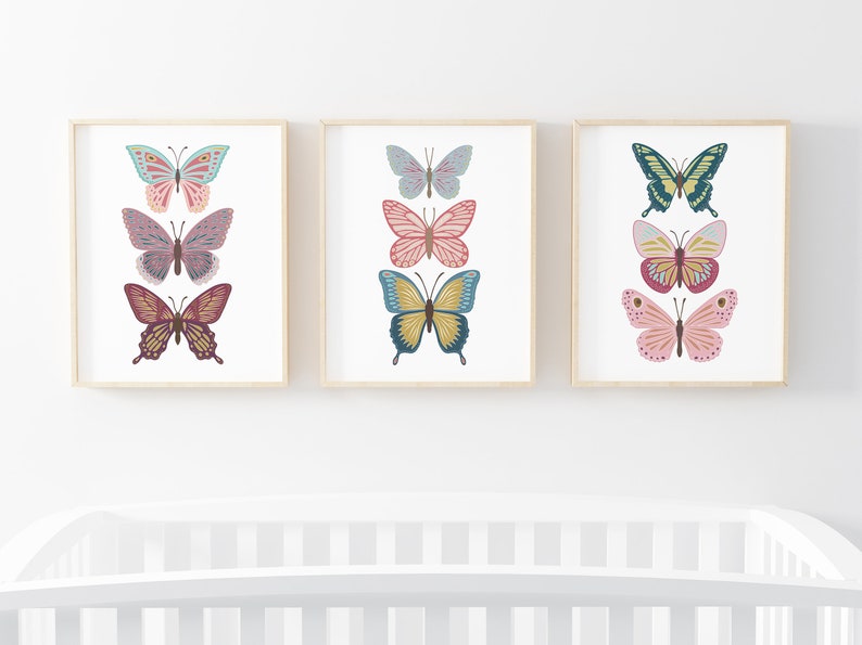 May include: Three framed butterfly art prints. Each print features three colorful butterfly illustrations in shades of pink, blue, yellow, and green. The artwork is displayed on a white background with a light wood frame.