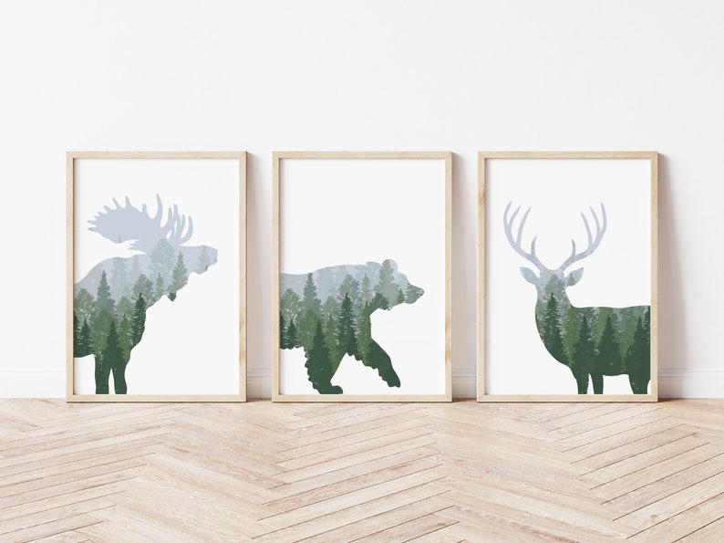 May include: Three framed art prints featuring silhouettes of a moose, bear, and deer. Each animal is filled with a forest scene in shades of green and gray. The frames are light brown, and the background is white.
