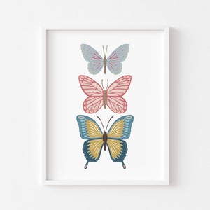 May include: A framed print featuring three colorful butterfly illustrations. The butterflies are arranged vertically, with a light blue butterfly at the top, a pink butterfly in the middle, and a blue and yellow butterfly at the bottom.