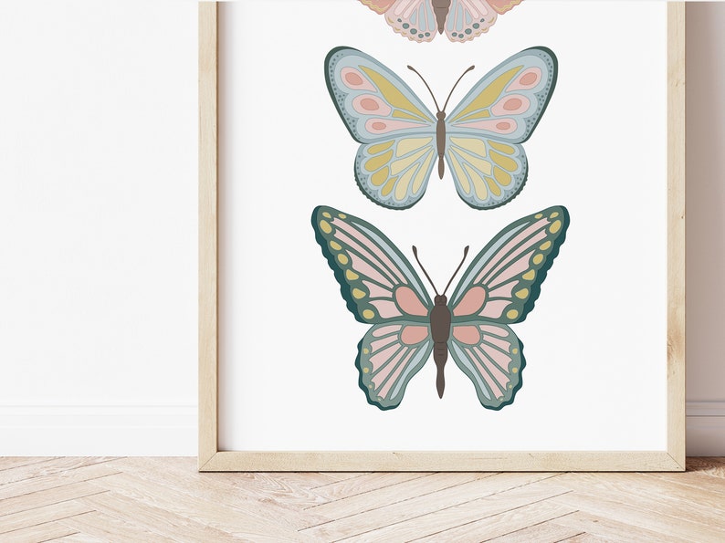 May include: A framed print featuring three colorful butterfly illustrations. The butterflies have detailed wing patterns in shades of pink, blue, yellow, and green. The artwork is set against a white background, and the frame is a light wood color.