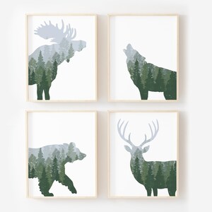 May include: Four framed art prints featuring forest animal silhouettes filled with a forest scene. The animals include a moose, a wolf, a bear, and a deer. The art prints have a white background and a light wood frame.