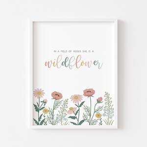 May include: White framed art print featuring the text "IN A FIELD OF ROSES SHE IS A wildflower" in pastel colors. The bottom of the print displays a colorful illustration of wildflowers in pink, yellow, and blue.