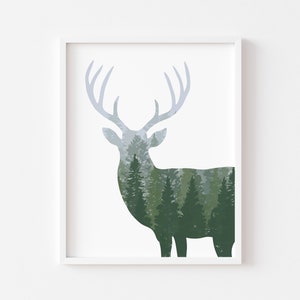 May include: A framed art print featuring a deer silhouette with a forest scene integrated into its form. The deer's antlers are a light blue-gray, and the forest is rendered in shades of green and gray. The artwork is set against a white background.