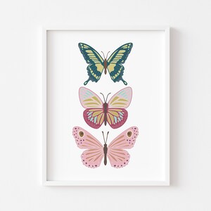 May include: A framed print featuring three colorful butterfly illustrations. The top butterfly is teal and yellow, the middle one is pink and yellow, and the bottom one is pink with brown spots. The butterflies are set against a white background.