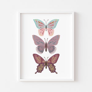May include: A framed print featuring three colorful butterfly illustrations. The butterflies are in shades of pink, blue, and purple, with intricate wing patterns. The artwork is set against a white background, creating a clean and modern aesthetic.