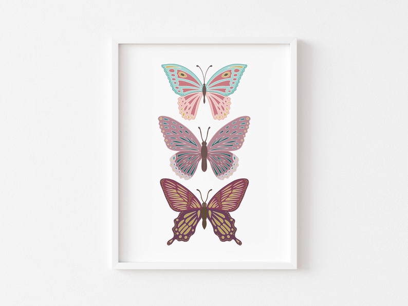 May include: A framed print featuring three colorful butterfly illustrations. The butterflies are in shades of pink, blue, and purple, with intricate wing patterns. The artwork is set against a white background, creating a clean and modern aesthetic.