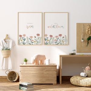 May include: Two framed art prints with floral designs and text. One reads "In a field of roses" and the other "She is a wildflower." The prints feature a pastel color palette and are displayed above a wooden chest.