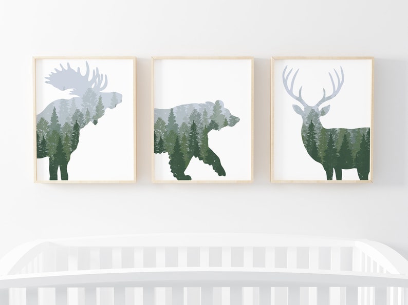 May include: Set of three framed art prints featuring silhouettes of a moose, bear, and deer. Each animal is filled with a forest scene in shades of green and gray. The frames are light wood, and the background is white.