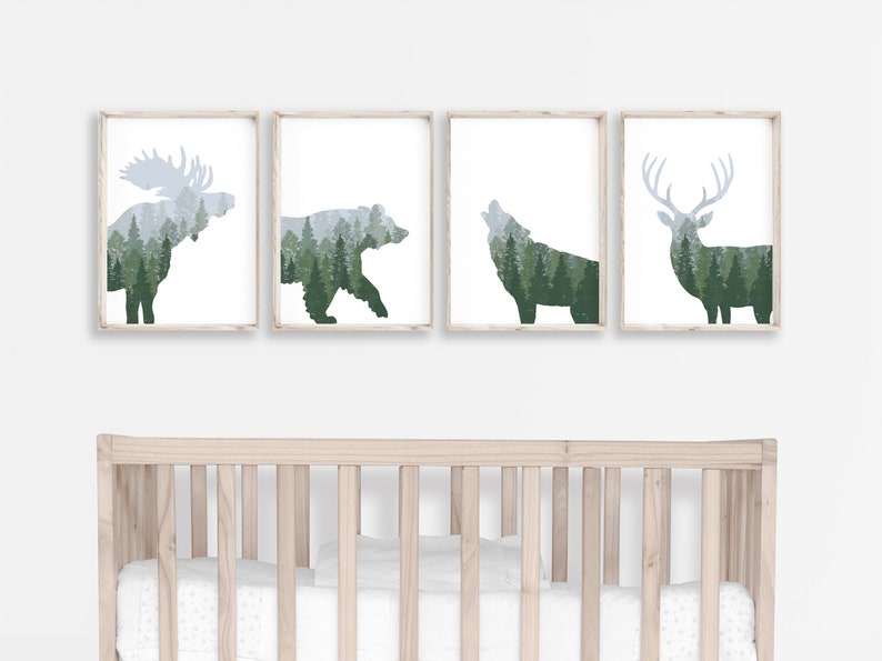 May include: Four framed art prints featuring forest animal silhouettes: a moose, bear, wolf, and deer. Each animal is filled with a green and gray forest scene. The prints are displayed above a light-colored wooden crib.