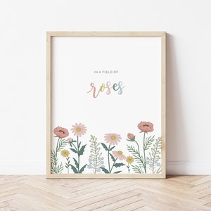 May include: A framed art print featuring a floral illustration. The artwork displays a field of flowers in pink, yellow, and blue hues, with the word "roses" in a pastel font. The frame is made of light-colored wood.