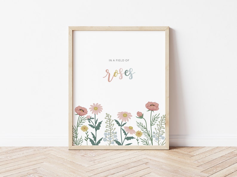 May include: A framed art print featuring a floral illustration. The artwork displays a field of flowers in pink, yellow, and blue hues, with the word "roses" in a pastel font. The frame is made of light-colored wood.