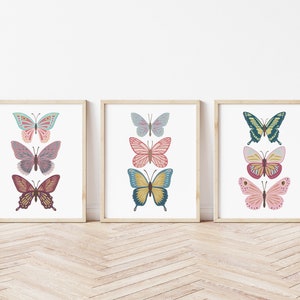 May include: Three framed butterfly art prints. Each print features three colorful butterfly illustrations in shades of teal, pink, yellow, and burgundy. The prints are displayed on a white background with a wooden frame.