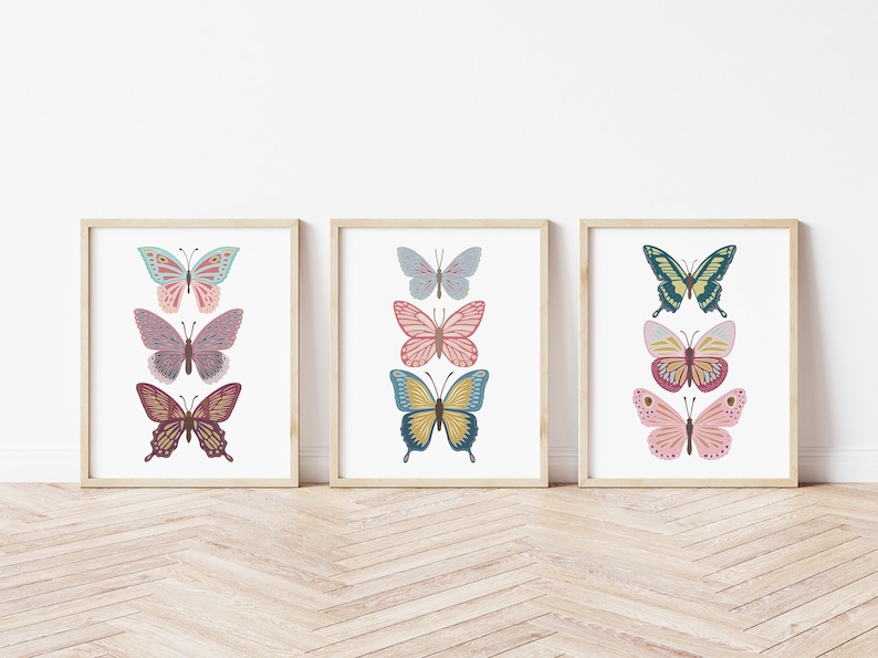 May include: Three framed butterfly art prints. Each print features three colorful butterfly illustrations in shades of teal, pink, yellow, and burgundy. The prints are displayed on a white background with a wooden frame.