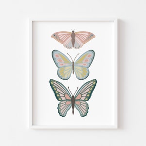 May include: A framed print featuring three stylized butterflies in soft pastel colors. The top butterfly is pink and brown, the middle one is yellow and blue, and the bottom one is pink and green. The artwork is set against a white background.