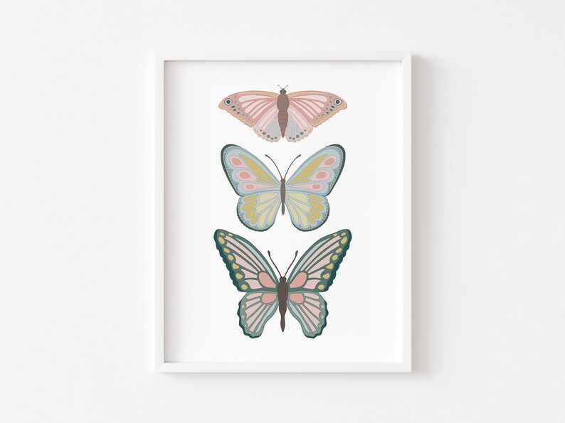 May include: A framed print featuring three stylized butterflies in soft pastel colors. The top butterfly is pink and brown, the middle one is yellow and blue, and the bottom one is pink and green. The artwork is set against a white background.