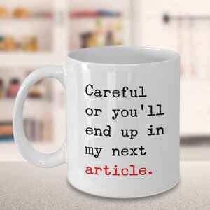 May include: White ceramic coffee mug with black text that reads "Careful or you'll end up in my next article." The word "article" is in red.