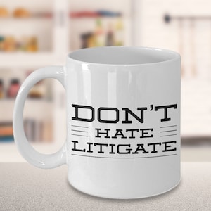 May include: White ceramic coffee mug with black text that reads "DON'T HATE LITIGATE".