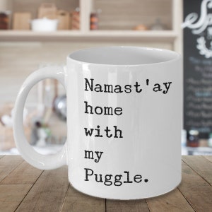 Puede incluir: Taza de café de cerámica blanca con texto negro que dice "Namaste'ay home with my Puggle."