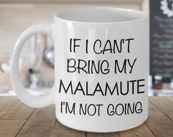 May include: White ceramic mug with a black handle. The mug features the text "IF I CAN'T BRING MY MALAMUTE I'M NOT GOING" in a black, bold font. The mug is on a wooden surface.