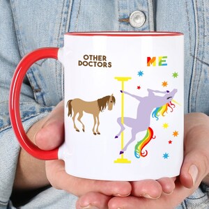 May include: White ceramic coffee mug with a red handle. The mug has a graphic of a horse and a unicorn. The text on the mug reads "Other Doctors" and "Me".