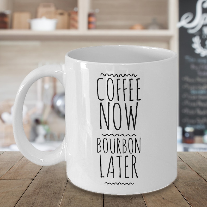 K&ouml;nnte beinhalten: Wei&szlig;e Keramik-Kaffeetasse mit schwarzem Text, der "Coffee Now Bourbon Later" lautet.