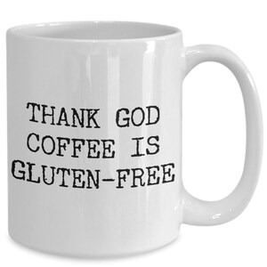 Puede incluir: Taza de caf&eacute; de cer&aacute;mica blanca con texto negro que dice "THANK GOD COFFEE IS GLUTEN-FREE".