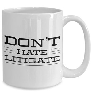 May include: White ceramic coffee mug with black text that reads "DON'T HATE LITIGATE".