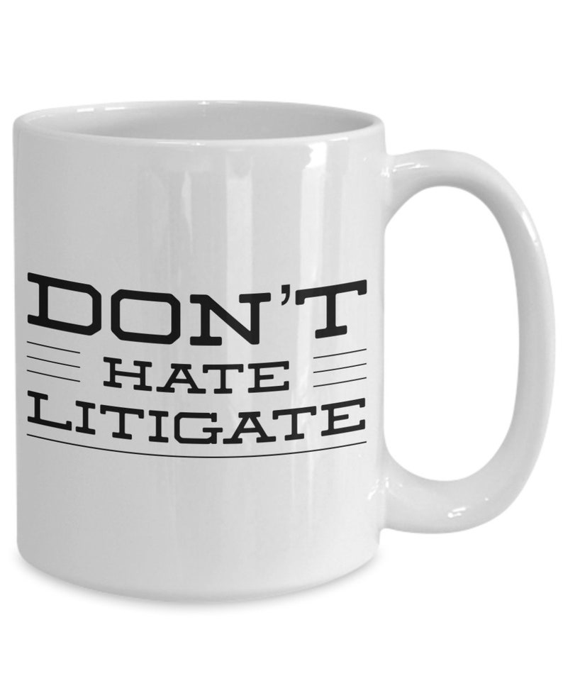 May include: White ceramic coffee mug with black text that reads "DON'T HATE LITIGATE".