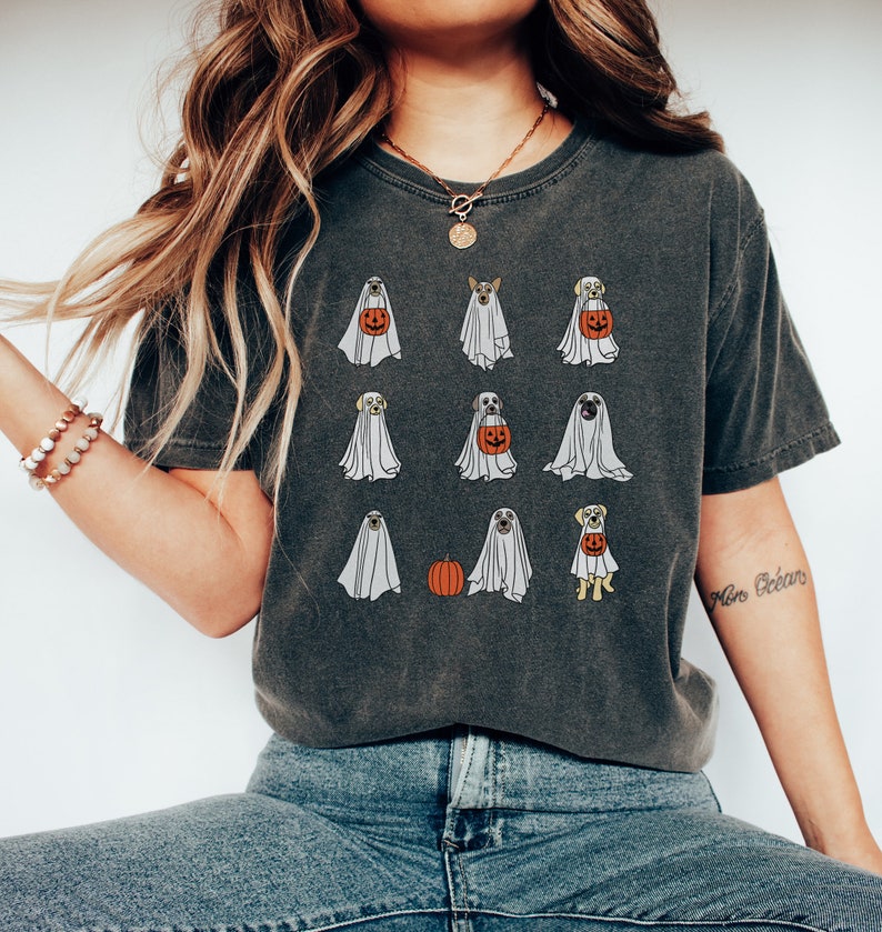 Peut inclure: Un t-shirt gris fonc&eacute; avec un imprim&eacute; graphique de chiens d&eacute;guis&eacute;s en fant&ocirc;mes pour Halloween. Les chiens portent des draps blancs et certains tiennent des citrouilles. Le t-shirt a un aspect vieilli.