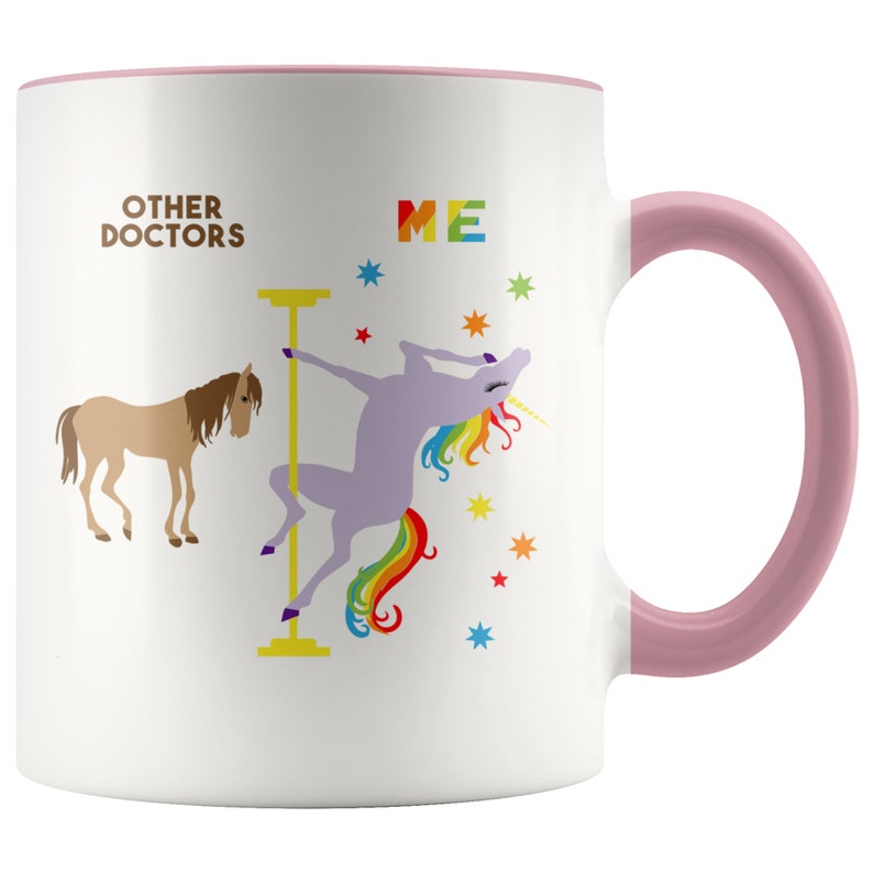 May include: White ceramic coffee mug with a pink rim and handle. The mug features a graphic of a unicorn with a rainbow tail, dancing on a pole. The text "OTHER DOCTORS" is on the left side of the mug and "ME" is on the right side.