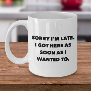 May include: White ceramic coffee mug with black text that reads "Sorry I'm late. I got here as soon as I wanted to."