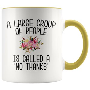 May include: White ceramic mug with a yellow rim and handle. The mug features a floral design and the text "A large group of people is called a "no thanks""