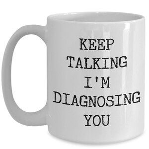 May include: White ceramic coffee mug with black text that reads "Keep Talking I'm Diagnosing You".