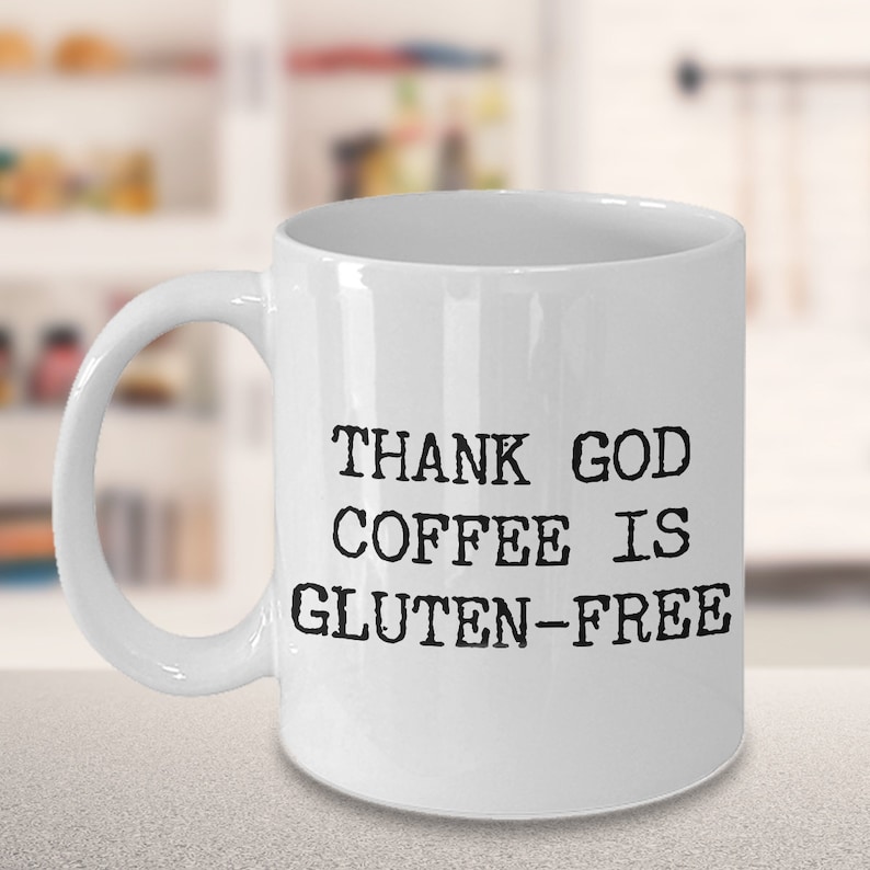Puede incluir: Taza de caf&eacute; de cer&aacute;mica blanca con texto negro que dice "THANK GOD COFFEE IS GLUTEN-FREE".