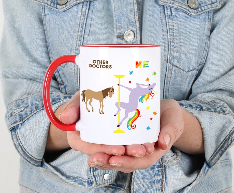 May include: White ceramic coffee mug with a red handle. The mug has a graphic of a horse and a unicorn. The text on the mug reads "Other Doctors" and "Me".