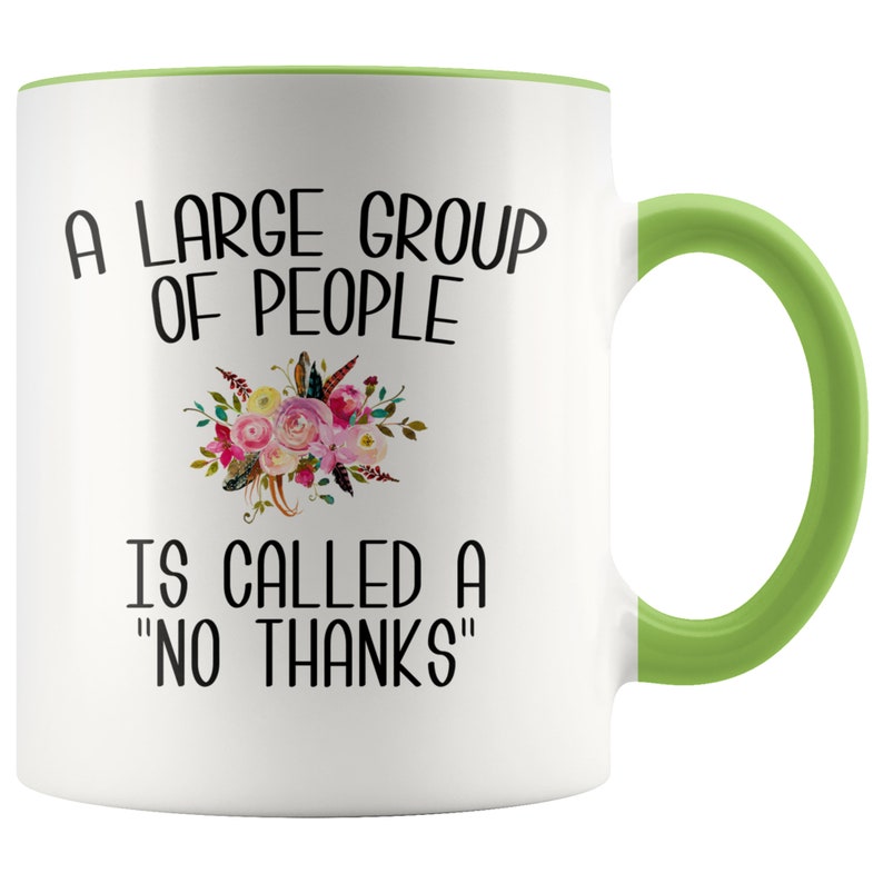 May include: White ceramic coffee mug with a green rim and handle. The mug features a floral design and the text "A large group of people is called a "no thanks""