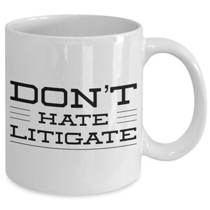 May include: White ceramic coffee mug with black text that reads "DON'T HATE LITIGATE".