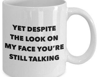 May include: White ceramic coffee mug with black text that reads "Yet despite the look on my face you're still talking".