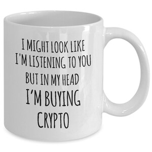 May include: White ceramic coffee mug with black text that reads "I might look like I'm listening to you but in my head I'm buying crypto."