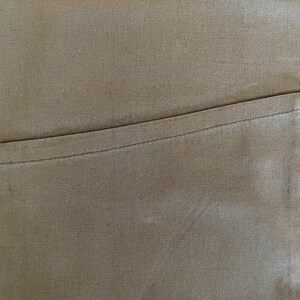 May include: A close-up of a brown fabric with a single pocket sewn on the right side.
