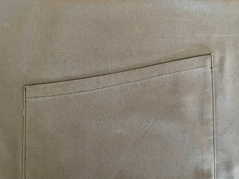 May include: A close-up of a brown fabric with a single pocket sewn on the right side.
