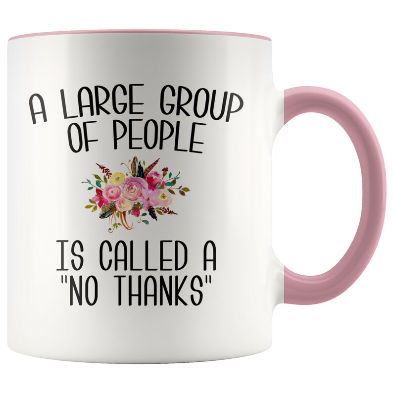 May include: White ceramic coffee mug with a pink rim and handle. The mug features a black and white graphic that reads "A large group of people is called a "no thanks"". The graphic is surrounded by a floral design.