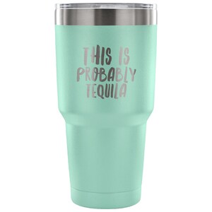 May include: A light green stainless steel tumbler with a silver lid. The tumbler has the text "This is probably tequila" printed on the side.