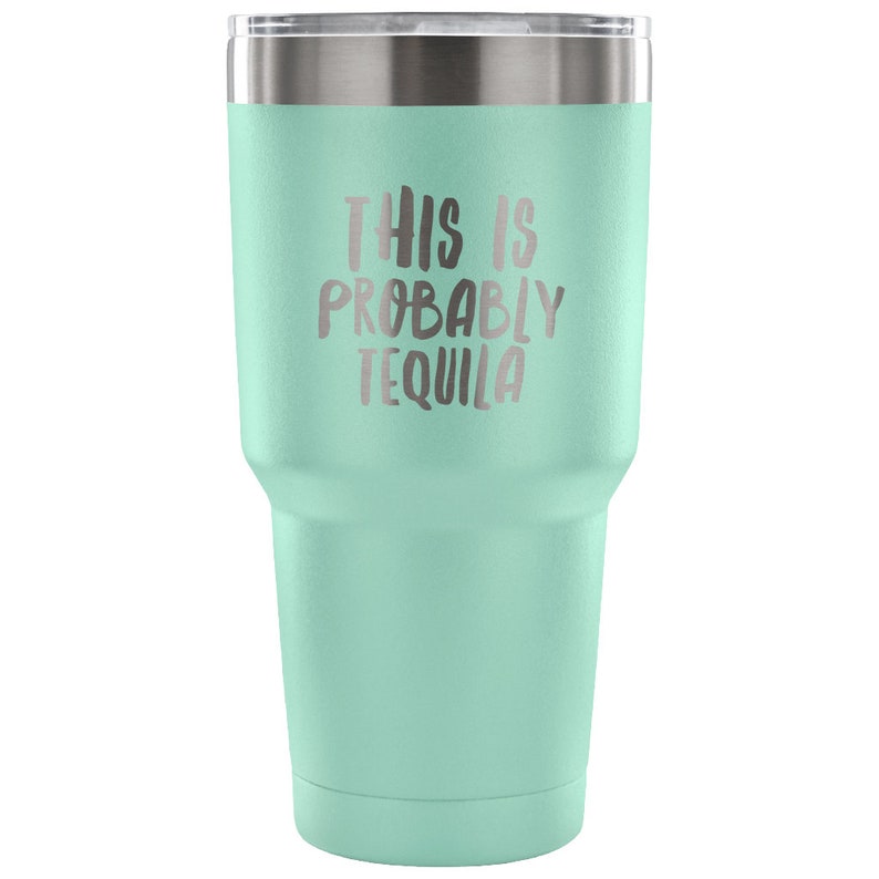 May include: A light green stainless steel tumbler with a silver lid. The tumbler has the text "This is probably tequila" printed on the side.
