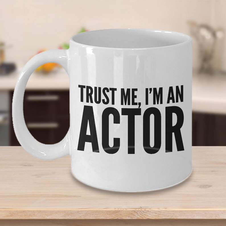 May include: White ceramic coffee mug with a black handle and the text "Trust me, I'm an actor" printed on the front.
