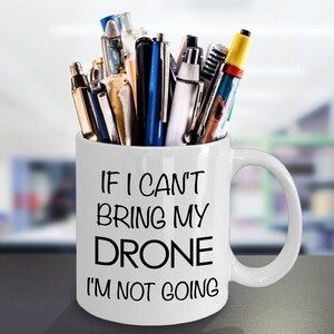 May include: White ceramic mug with a black inscription that reads "If I can't bring my drone I'm not going". The mug is filled with pens and pencils.