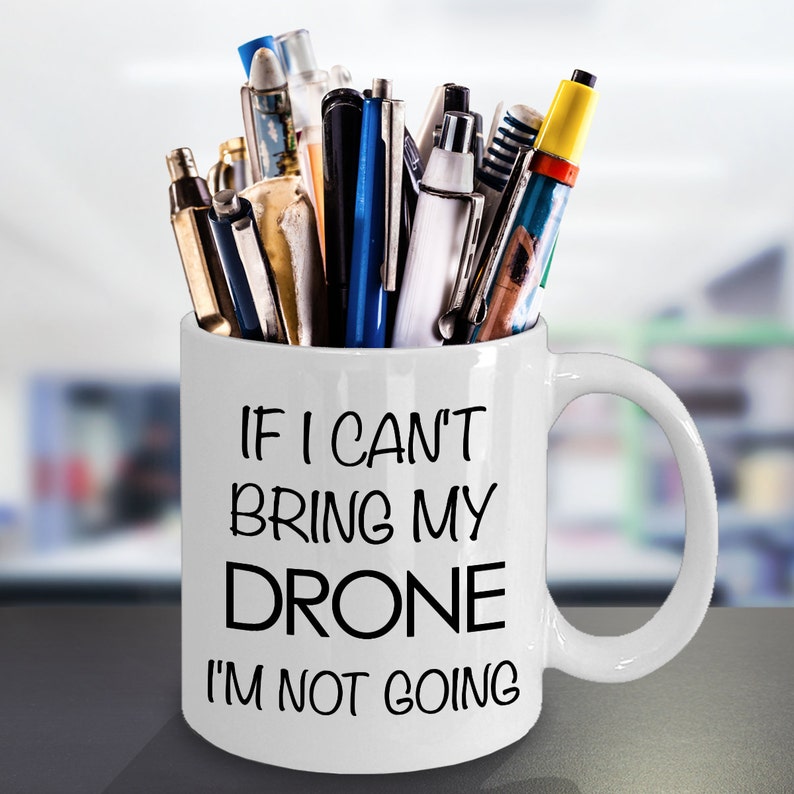 May include: White ceramic mug with a black inscription that reads "If I can't bring my drone I'm not going". The mug is filled with pens and pencils.
