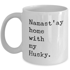 May include: White ceramic coffee mug with black text that reads "Namaste'ay home with my Husky."