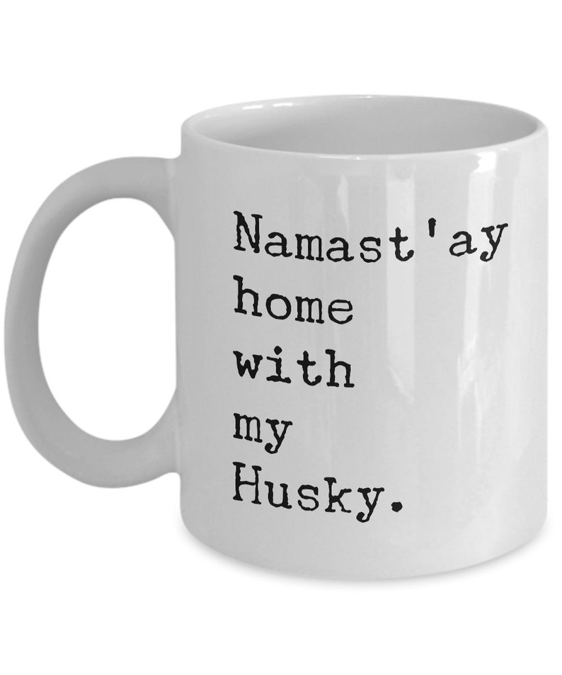 May include: White ceramic coffee mug with black text that reads "Namaste'ay home with my Husky."