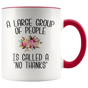May include: White ceramic coffee mug with a red rim and handle. The mug features a black and white graphic that reads "A large group of people is called a "no thanks"".  The graphic is surrounded by a floral design.